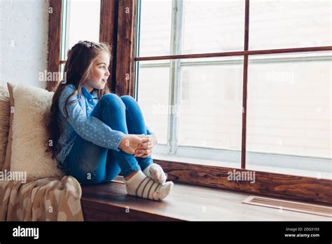 Sad Little Girl Sitting On Window Sill Looking At Street During