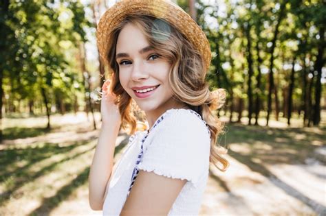 Free Photo Blissful Blonde Girl In Straw Hat Playfully Posing In Forest Outdoor Shot Of