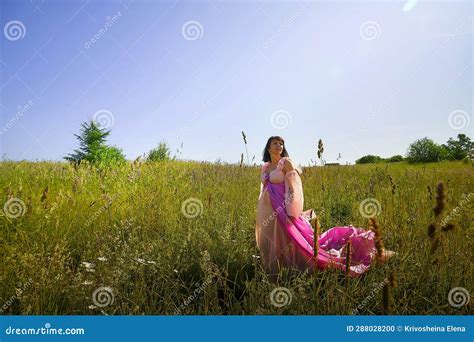 Beautiful Girl In A Lush Pink Ball Gown In Green Field During Blooming