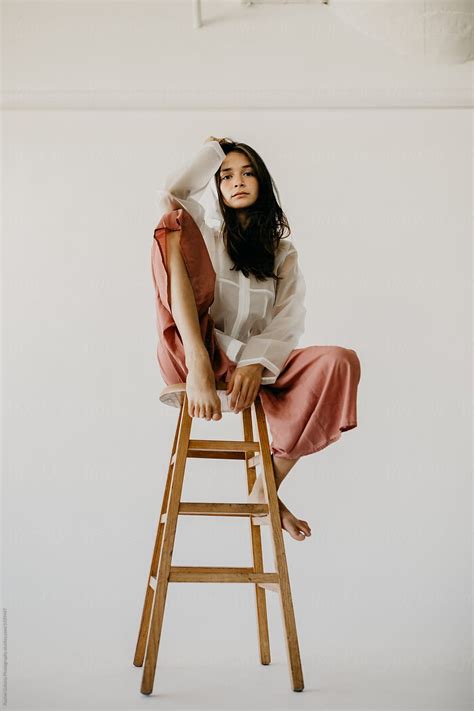 woman model posing on a stool in culottes and a raincoat stocksy united model poses