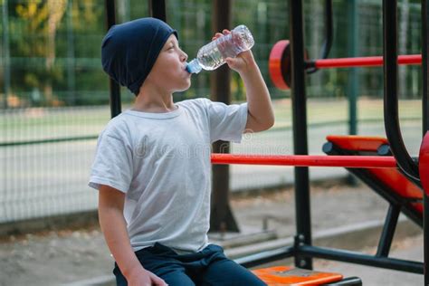 Little Boy Drinking Water Near Outdoor Public Fitness Equipment Stock