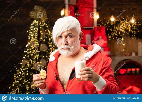 Modern Santa Claus Eating A Cookie And Drinking Glass Of Milk At Home