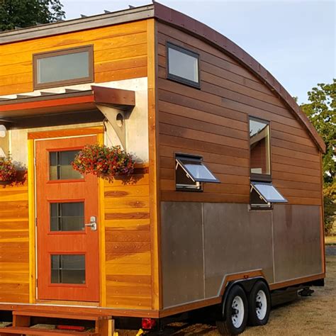 A Tiny House On Wheels Is Parked In The Grass With Flowers Growing Out Of It S Windows