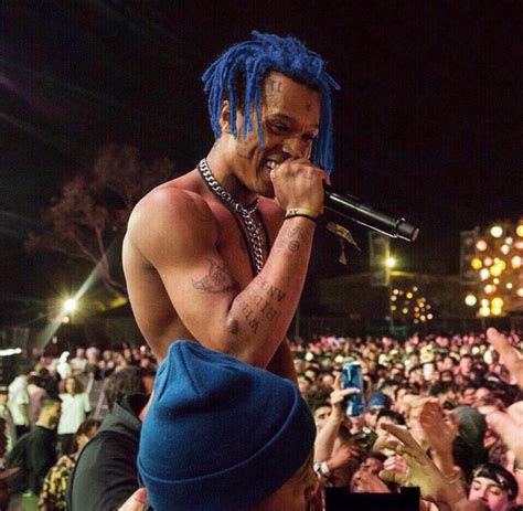 A Man With Blue Dreadlocks On His Head Singing Into A Microphone