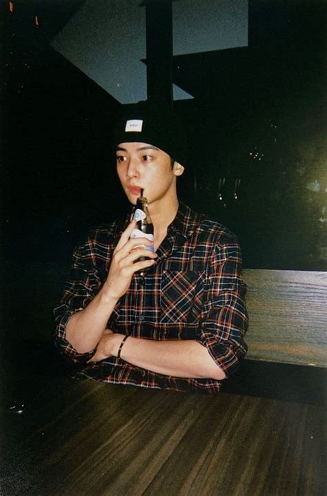 A Man Sitting At A Table With A Bottle In His Hand And Wearing A Hat