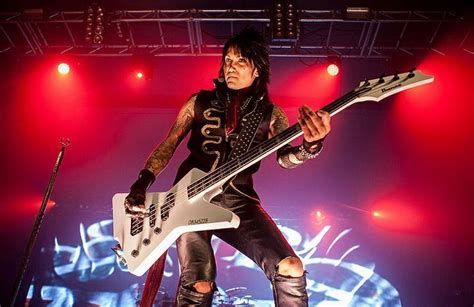 a man with black hair and piercings holding a white guitar in front of red lights