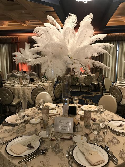 The Table Is Set With White Feathers And Place Settings