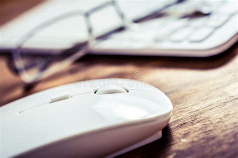 White Computer Mouse Lying Next To Glasses And White Keyboard On Wooden