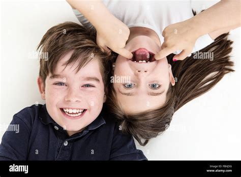 Cheeky Children Pulling Funny Faces At Each Other Whilst Laying On The