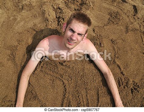 Picture Of Young Man Buried In The Sand On The Beach Smiling Up At The