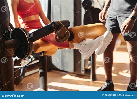 Crop Sportswoman Exercising On Leg Extension Machine With Trainer Stock