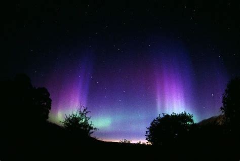 The Aurora Bore Is Visible In The Night Sky Over Trees And Hills With