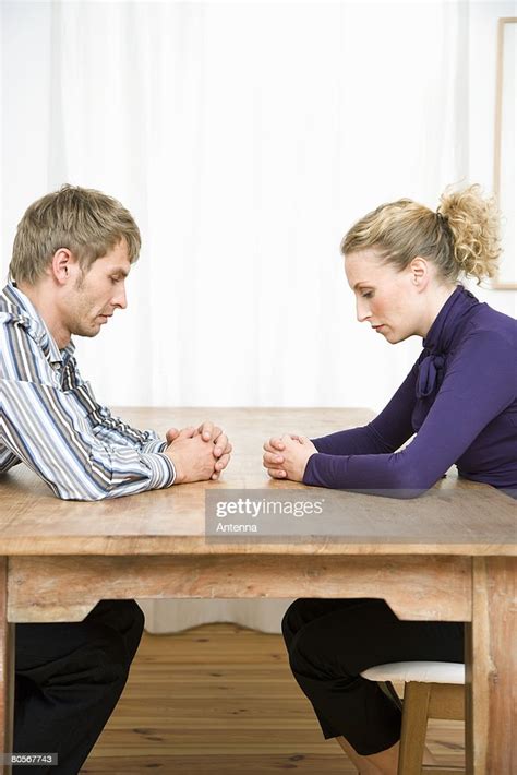 A Couple Sitting Opposite Each Other At A Table And Looking Sad Stock