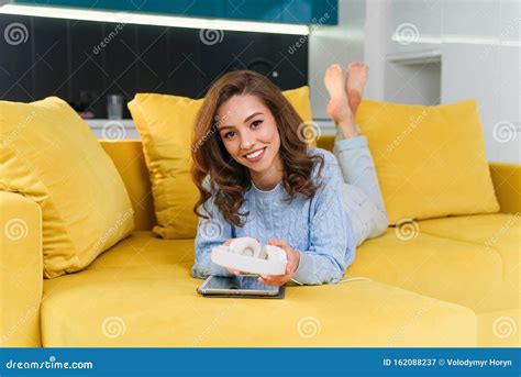 Satisfied Happy Girl Using Tablet While Lying On Comfortable Yellow
