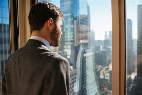 Young Businessman Looking Out Of A Window In An Office In Tall