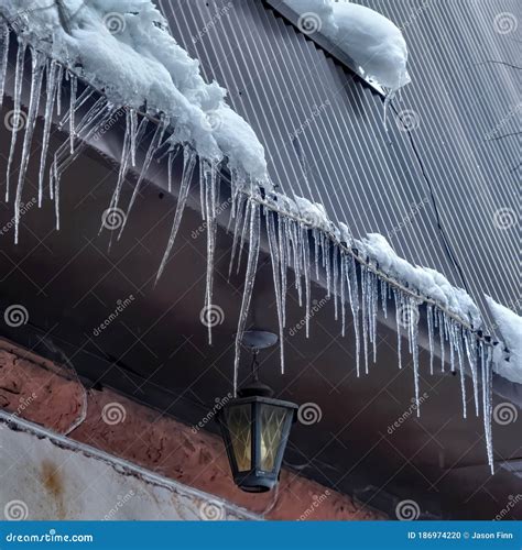 Square Spiked Icicles At The Edge Of Pitched Gray Roof With Clumps Of