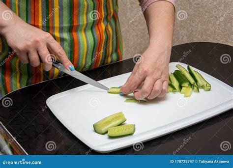 closeup hands girl in a striped apron in the kitchen is slicing cucumbers into strips on a