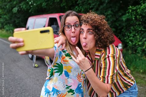 Two Girls Taking A Selfie With Their Phone Sticking Out Their Tongues During A Road Trip Stock