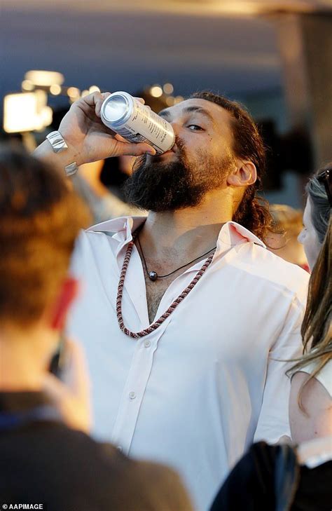 A Man With Long Hair Drinking From A Bottle While Standing In Front Of Other People