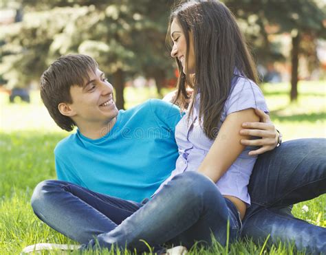 Romantic Young Couple Sitting Together At Park On The Grass And Stock