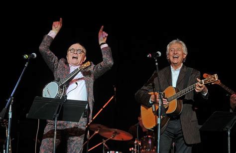 Two Men Singing And Playing Guitars On Stage With Their Hands In The