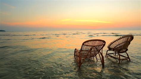 Sunset On A Beach Two Empty Wooden Chairs Standing In A Water Stock