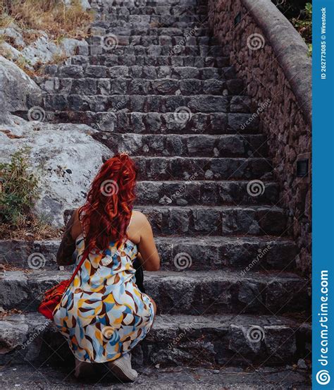 Vertical Shot Of A Female With Red Hair Sitting Near A Stairway Stock