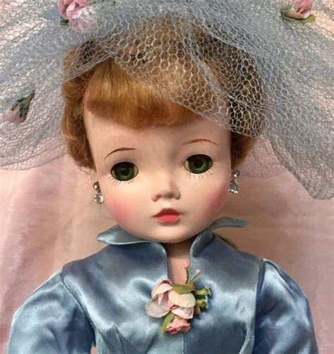 A Close Up Of A Doll Wearing A Blue Dress And Hat With Flowers On It