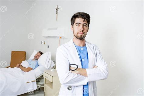 Young Doctor At Hospital Bedroom With Sick Patient Lying In Bed Stock