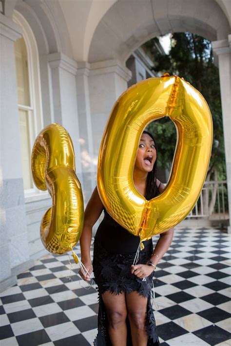 A Woman In A Black Dress Holding Two Gold Balloons That Spell Out The Number 50