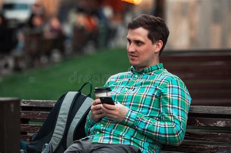 Portrait Of Young Handsome Man Sitting On Bench Drinking Coffee