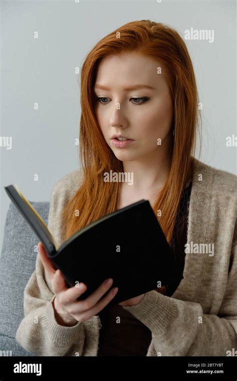 A Beautiful Red Haired Girl Carefully Reads A Black Book Holding Her In