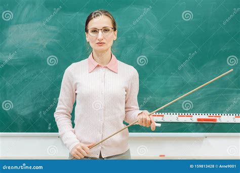 Strict Teacher Standing In Front Of Blackboard In Class Stock