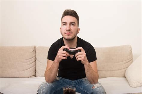 Premium Photo Young Gamer Sitting On Sofa And Playing Video Games At Home