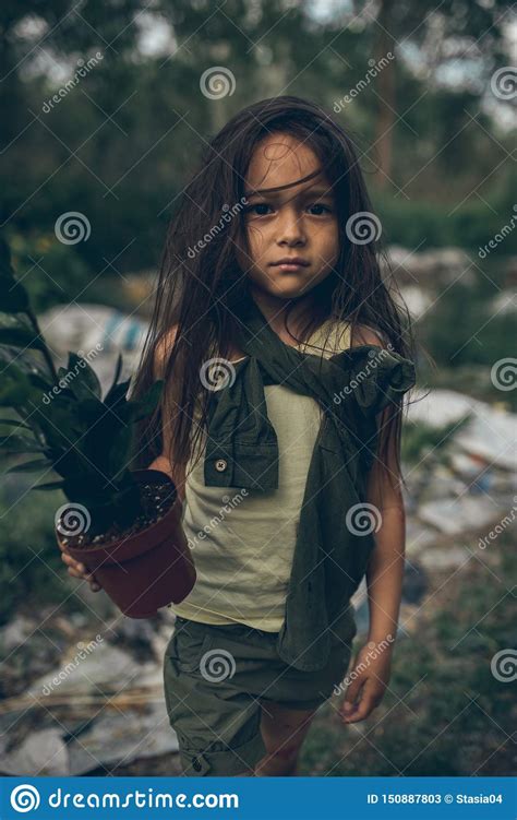 A Homeless Girl Is Standing On A Garbage Dump With A Houseplant In A