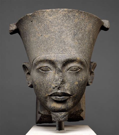 the head of an ancient egyptian statue is displayed on a white pedestal in front of a gray