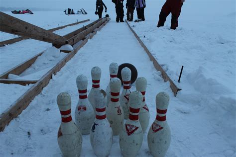 Several People Standing Around Bowling Pins In The Snow
