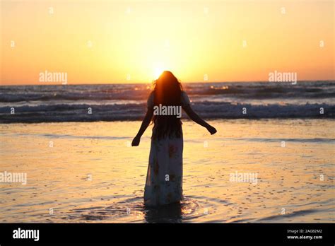 Woman Wading In Water At The Beach With Sunset In Background Stock