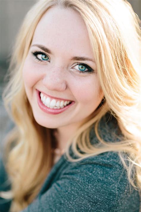 A Close Up Of A Person With Blonde Hair And Blue Eyes Smiling At The Camera