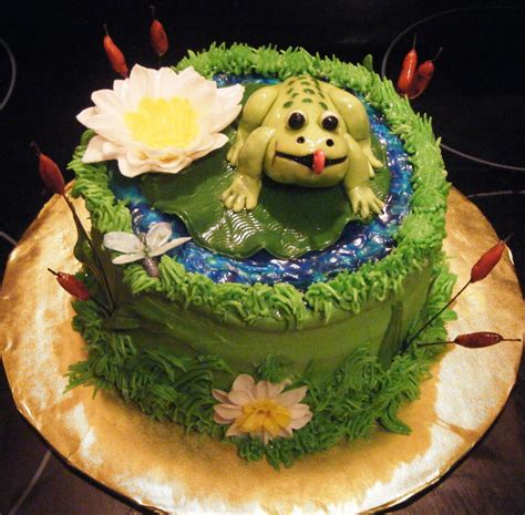 a green cake with a frog in the center and flowers on it s side