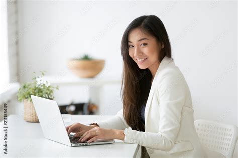 Portrait Of Beautiful Asian Female Office Worker Looking At Camera Smiling While Working At