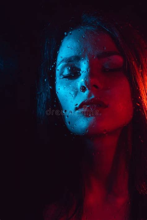 Sensual Portrait Of Beautiful Girl Behind Glass With Raindrops With Red Blue Lighting Stock
