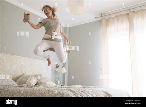 Young Adult Pretty Woman Go Crazy For Happiness And Jump On The Bed With Coffee Cup Overjoyed