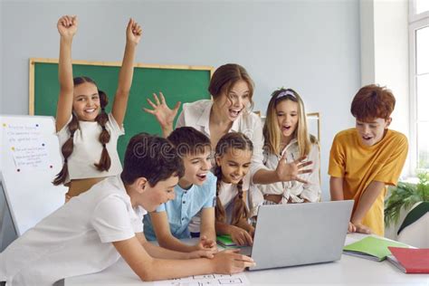 Group Of Happy Excited School Children And Teacher Using Laptop And