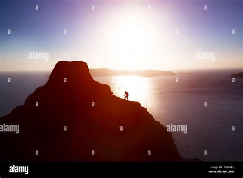 Man Climbing Up Hill To Reach The Peak Of The Mountain Over Ocean Stock