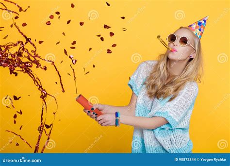 Portrait Of Funny Blond Woman In Birthday Hat And Red Confetti On Yellow Background Celebration