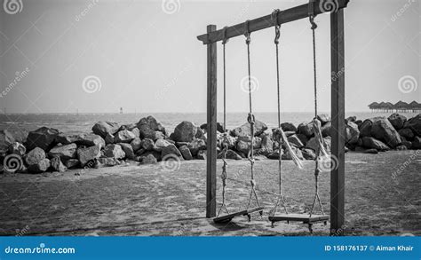 Black And White Of An Old Swing At The Beach With Beach Rocks As