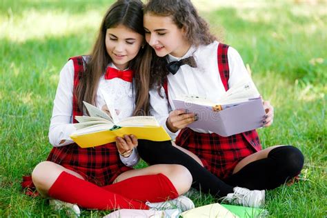 Zwei Schulmädchen In Den Roten Schuluniformen Sitzen Auf Einem Grünen Rasen Mit Büchern