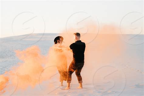 Guy And A Girl In Black Clothes Hug And Run On The White Sand With Orange Smoke By Andrii