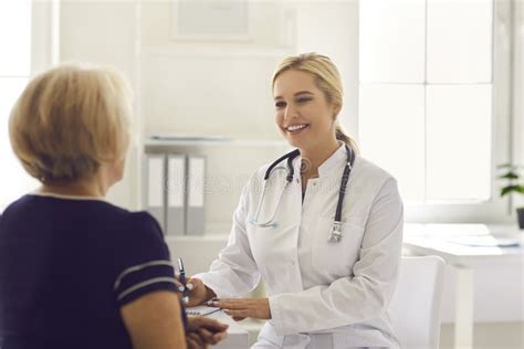 Woman Doctor Sitting And Making Notes During Consultation With Mature